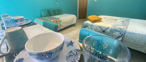 A room with two beds, a TV mounted on the wall, and a table with a bowl and a cup.
