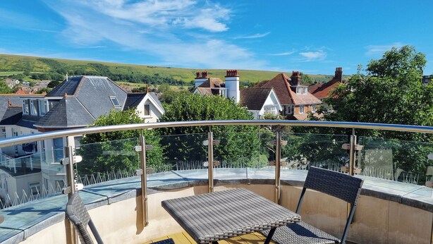 A balcony with a glass railing, two chairs, and a table. - Number 10 The Penthouse (Swanage)