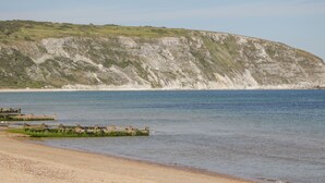 A coastal landscape with a sandy beach, calm sea, and a large cliff with vegetation. - Number 10 The Penthouse (Swanage)