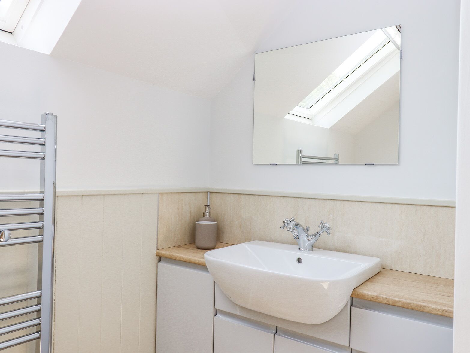 Een moderne badkamer met dakraam, een witte wastafel en een spiegel.