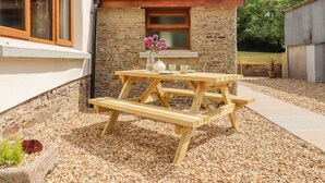 Une table de pique-nique en bois, avec un mur de pierres et une fenêtre en arrière-plan.