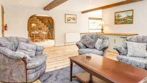 Un salon chaleureux avec des canapés à motifs, une table basse en bois et un escalier menant à une salle à manger.