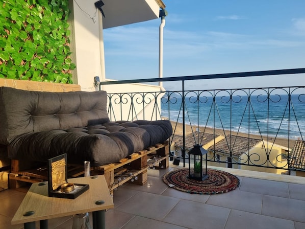 Ein Balkon mit gepolsterten Sitzgelegenheiten, einem kleinen Tisch mit Buddha-Statue und Blick auf den Ozean.
