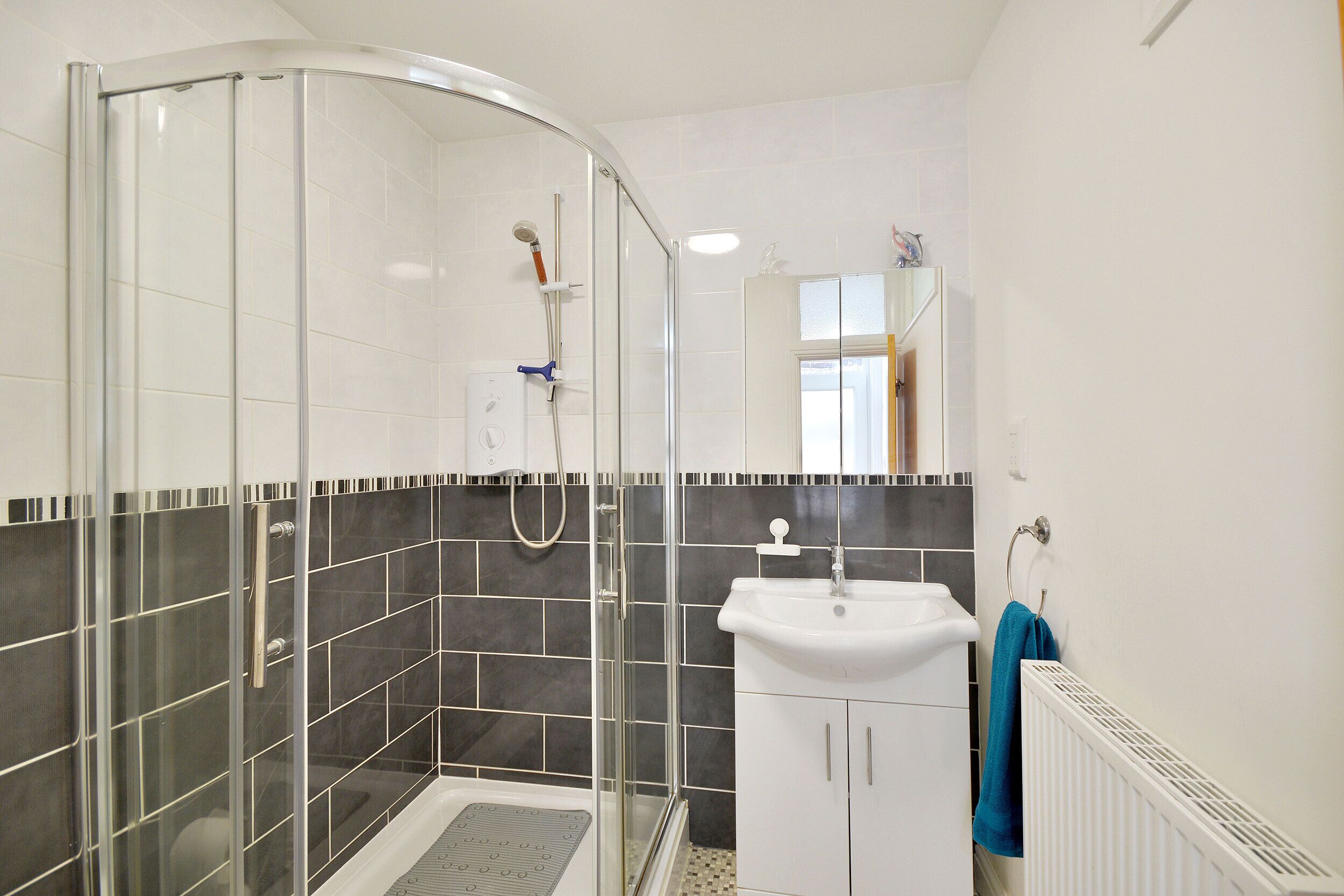 Un baño moderno con cabina de ducha de vidrio, lavamanos blanco y suelo de baldosas.