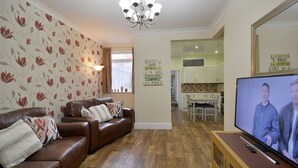 A living room with a brown leather sofa, a flat-screen TV, and a wooden entertainment unit. - Brightwater Ground Floor Apartment up to 6 Guests (Scarborough)