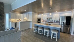 A modern kitchen with white cabinets, a stainless steel refrigerator, and a bar area with stools. - Beautiful lakefront property with hot tub  (Leesburg)