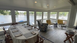 A dining area with a large table and chairs, large windows with a view of a lake and boats, and a wooden floor. - Beautiful lakefront property with hot tub  (Leesburg)