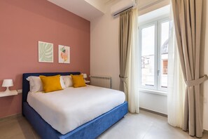 Une chambre avec un grand lit, un radiateur, une fenêtre avec des rideaux et des œuvres d’art accrochées au mur.