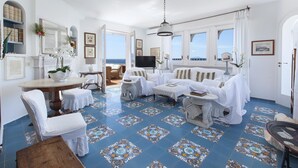 A spacious living room with a large window overlooking the sea, a round dining table, and a cozy seating area with a sofa and armchairs. - Villa Bouganville in Massa Lubrense (Massa Lubrense)