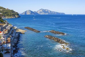 Un pueblo costero con un litoral rocoso, edificios a lo largo del mar y montañas al fondo.