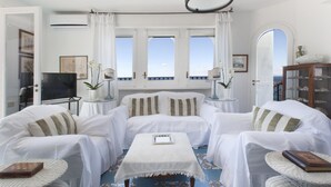 A living room with white furniture, a television, and a view through the windows. - Villa Bouganville in Massa Lubrense (Massa Lubrense)