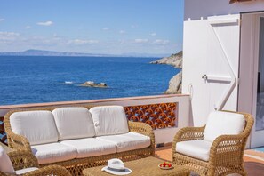 Un balcón con mobiliario de mimbre, una puerta blanca y vista al mar.