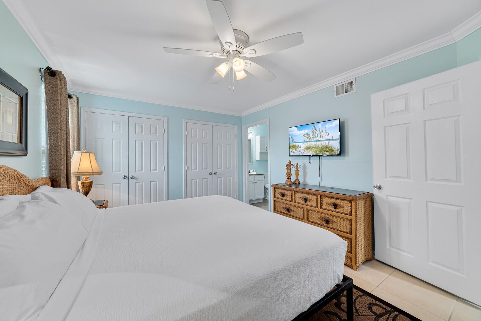 A bedroom with a bed, a ceiling fan, a dresser, and a television on the wall.