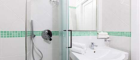 A bathroom with a glass shower enclosure, a white sink, and a mirror above the sink.