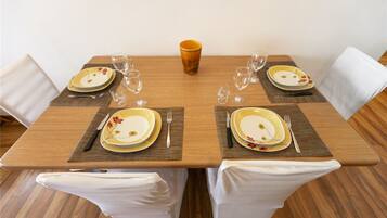 Mesa de comedor preparada para cuatro, con sillas blancas, una taza anaranjada en el centro y vajilla con motivos florales.