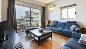 A modern living room with a sofa, a glass coffee table, a TV, and a balcony with a view of buildings.