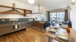 A modern kitchen with a dining area, wooden flooring, and a view of the city through large windows.