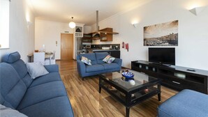 A modern living room with a sofa, coffee table, and TV stand. There is a kitchen area in the background with a microwave and cabinets.