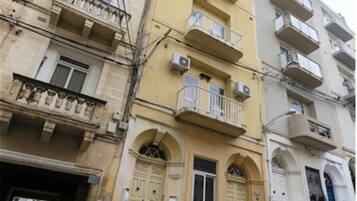 Un edificio de varios pisos con balcones, un coche estacionado al frente y una señal de calle a la vista.