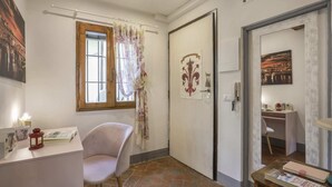 Une pièce comprenant un bureau, une chaise et une porte ornée d’un motif décoratif. Il y a une fenêtre avec un rideau et un tableau accroché au mur.