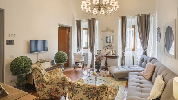 Un salon comprenant un canapé, des fauteuils, une table basse, un lustre, un téléviseur et une plante en pot.