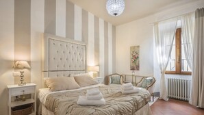 Une chambre d’hôtel avec un grand lit, des murs à rayures, un lustre, une fenêtre avec des rideaux et un radiateur.