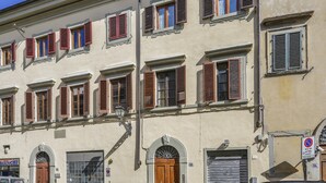 Un immeuble à plusieurs étages, doté d’arcades au niveau des portes et de fenêtres avec volets.