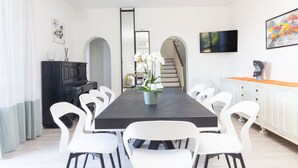 A modern dining room with a long table, white chairs, a potted orchid, a black cabinet, and a television on the wall. - Villa Luisa Jacuzzi Pool (Sorrento)