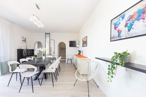 A modern dining area with a long table, white chairs, and a decorative plant.