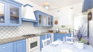 A kitchen with blue cabinets, a stove, and a dining area with a striped tablecloth. - Villa Luisa Jacuzzi Pool (Sorrento)