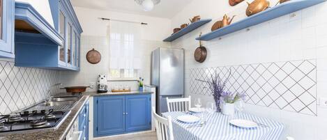 A modern kitchen with blue cabinets, a stainless steel refrigerator, and a dining area with a striped tablecloth.