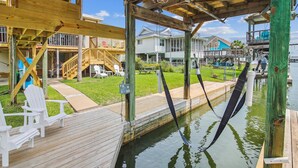 A wooden deck with white chairs, a small pool, and a covered area with a wooden railing. - Casa Hermosa by Ryson Vacation Rentals (Galveston)