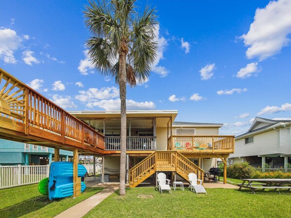 A two-story house with a covered deck, a palm tree, and a picnic table.