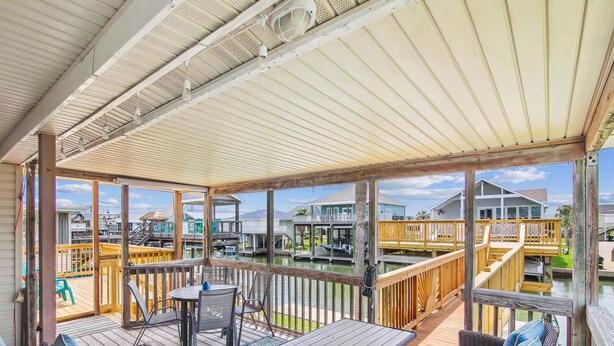 A covered outdoor deck with wicker furniture and a view of a marina. - Casa Hermosa by Ryson Vacation Rentals (Galveston)