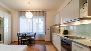 Una cocina moderna con armarios blancos, un comedor con mesa y sillas, y un amplio ventanal con cortinas.