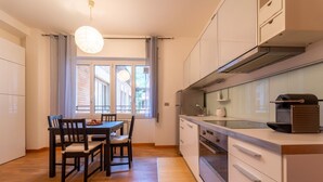 Cocina compacta con comedor, que incluye una mesa y sillas de madera, una estufa moderna y un ventanal con cortinas.
