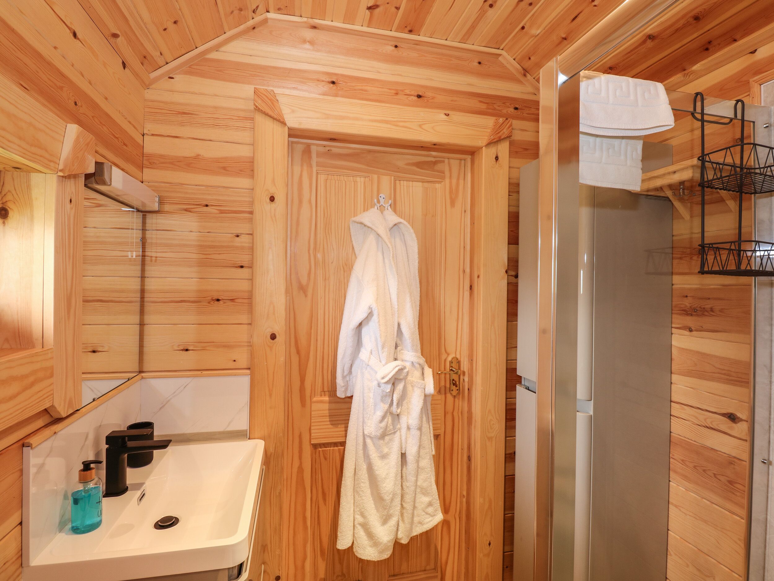 A wooden cabin bathroom with a sink, towel rack, and a shower area.