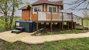 Une cabane en bois dotée d’une terrasse et d’un jacuzzi, entourée d’arbres et d’une zone herbeuse.