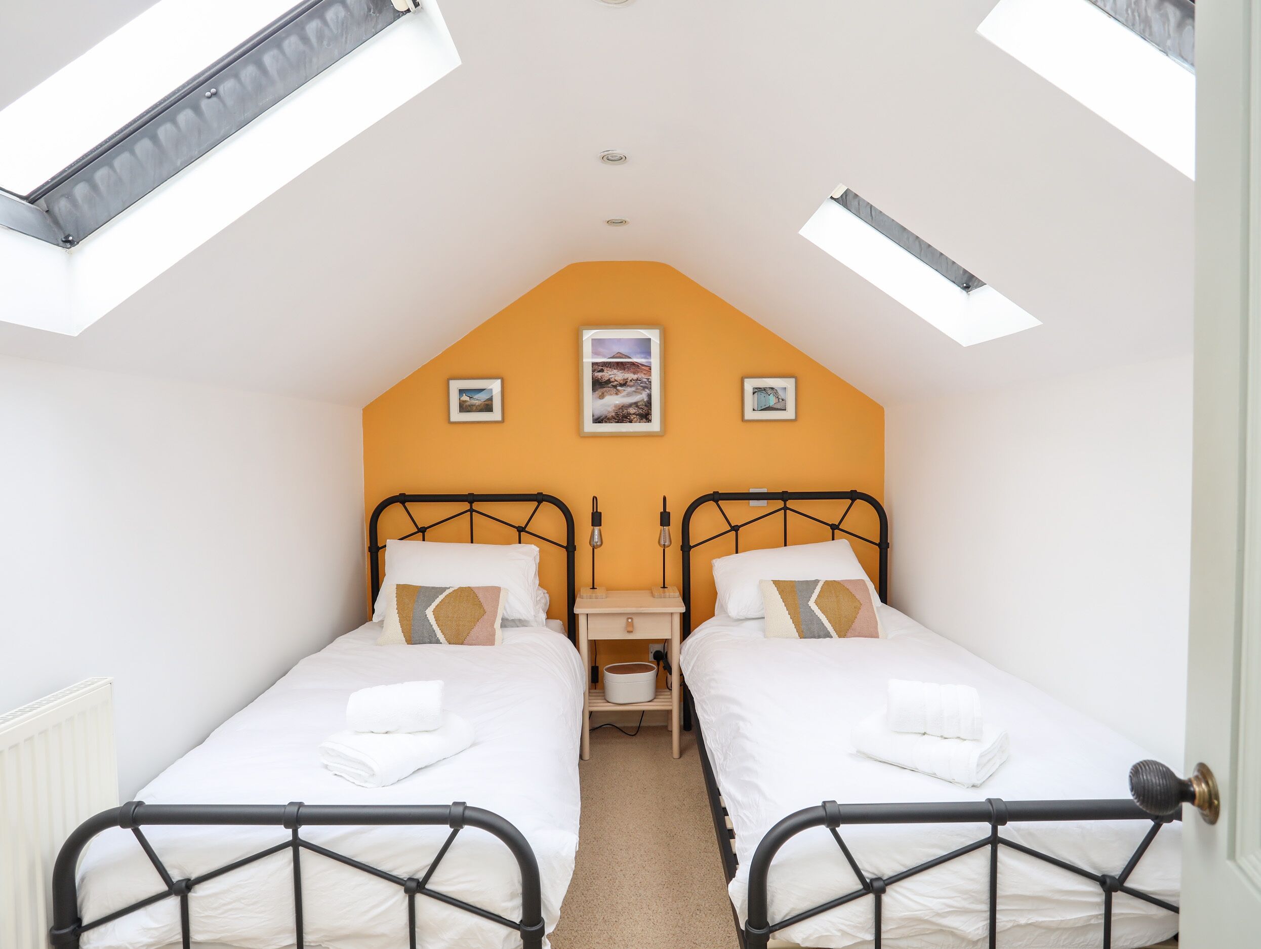 A bedroom with two beds, a skylight, and a small bedside table with a lamp.