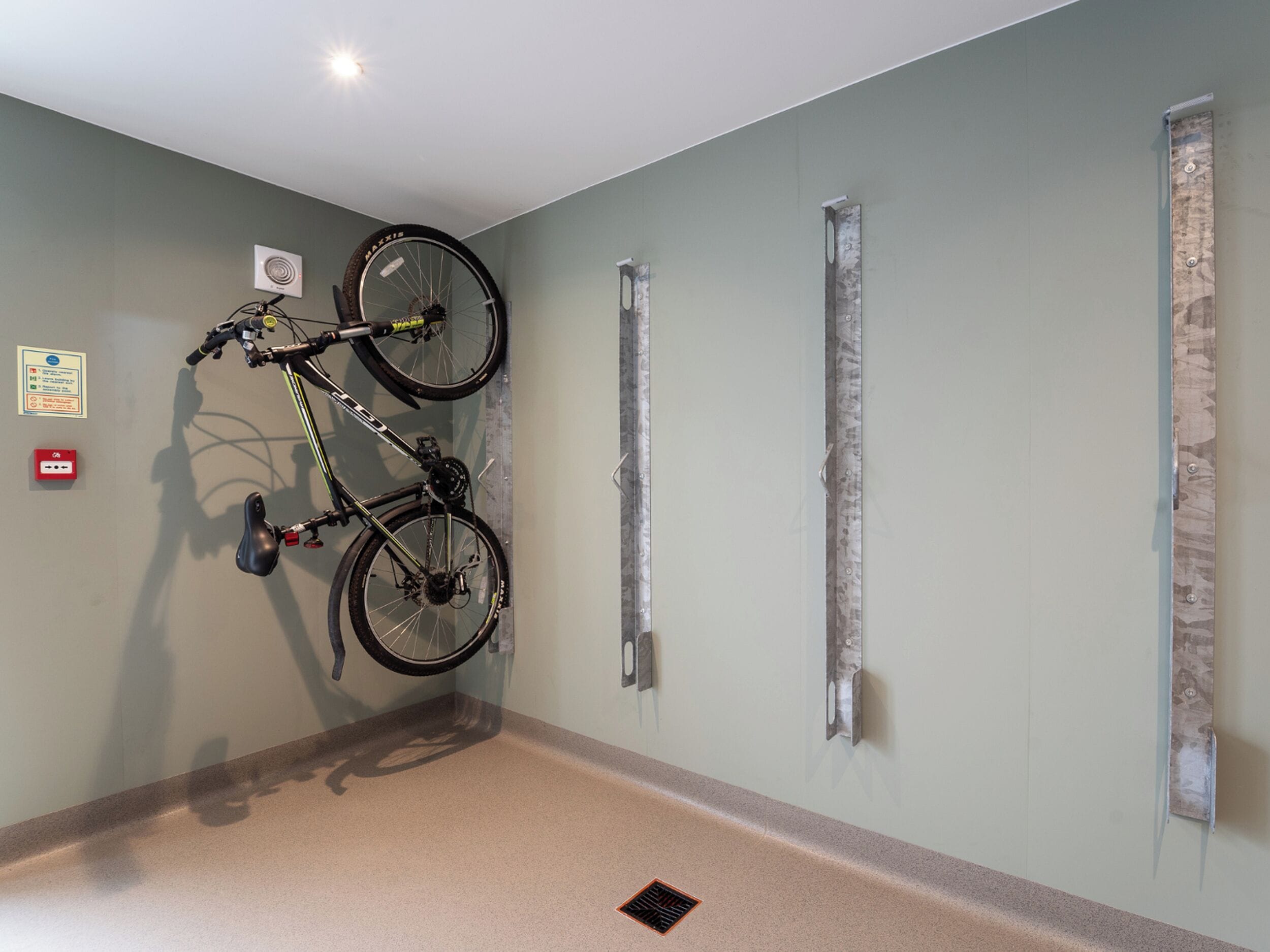 A room with a bicycle mounted on a wall, a fire alarm, and a vent.