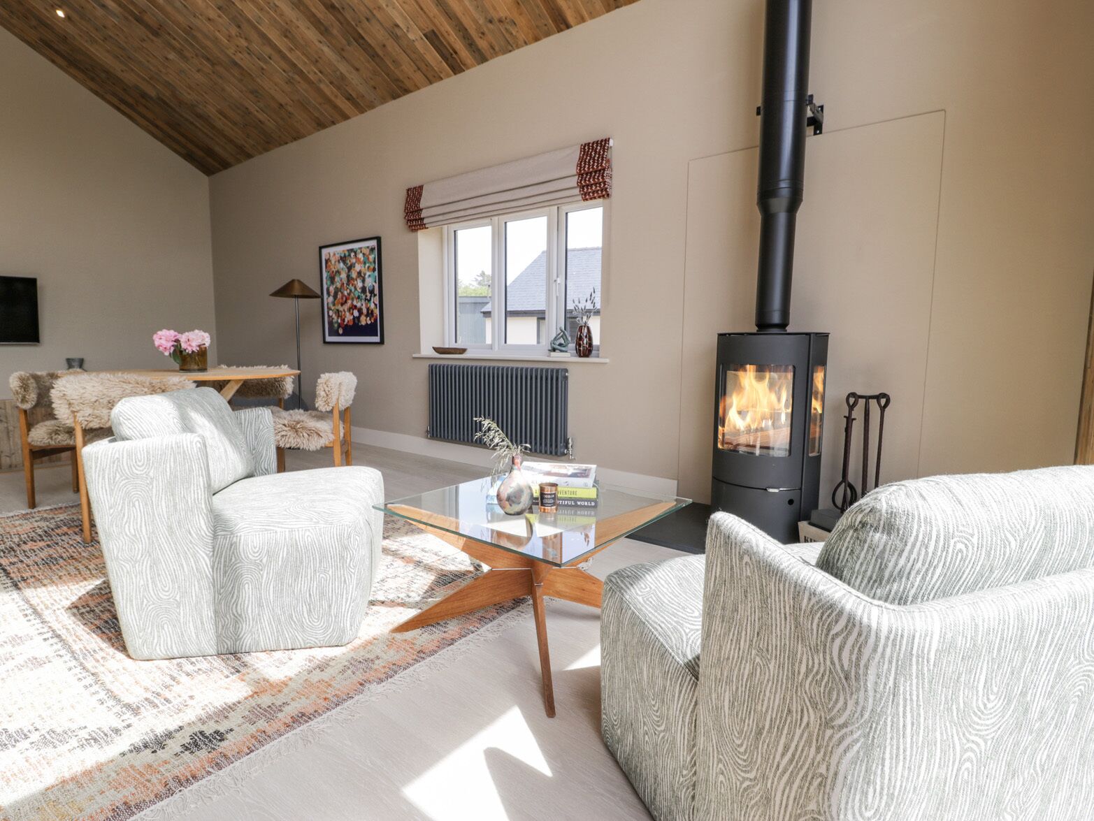 Una sala de estar acogedora con chimenea moderna, asientos confortables y un ventanal que deja entrar mucha luz natural.