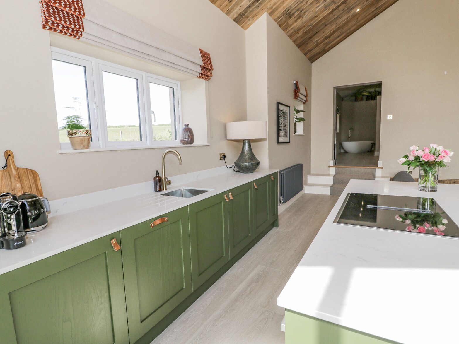 A modern kitchen with green cabinets, a white countertop, a sink, and a window overlooking a garden.