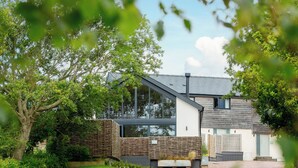 A modern house with a sloped roof, large windows, and a gravel driveway. - The Barn (Amlwch)