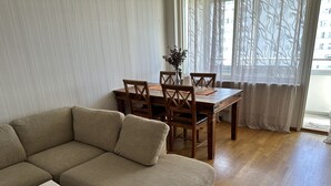 Una sala de estar con un sofá color beige, una mesa de comedor de madera con sillas y un jarrón con flores.
