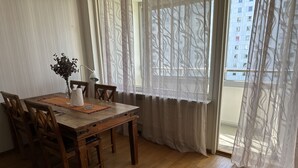 Un comedor con mesa de madera, sillas, un florero y cortinas translúcidas.