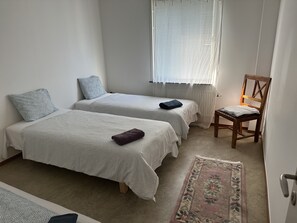 A bedroom with two single beds, a wooden chair, a patterned rug, and a window with blinds. - 3 Room Apartment in Solna (Solna)