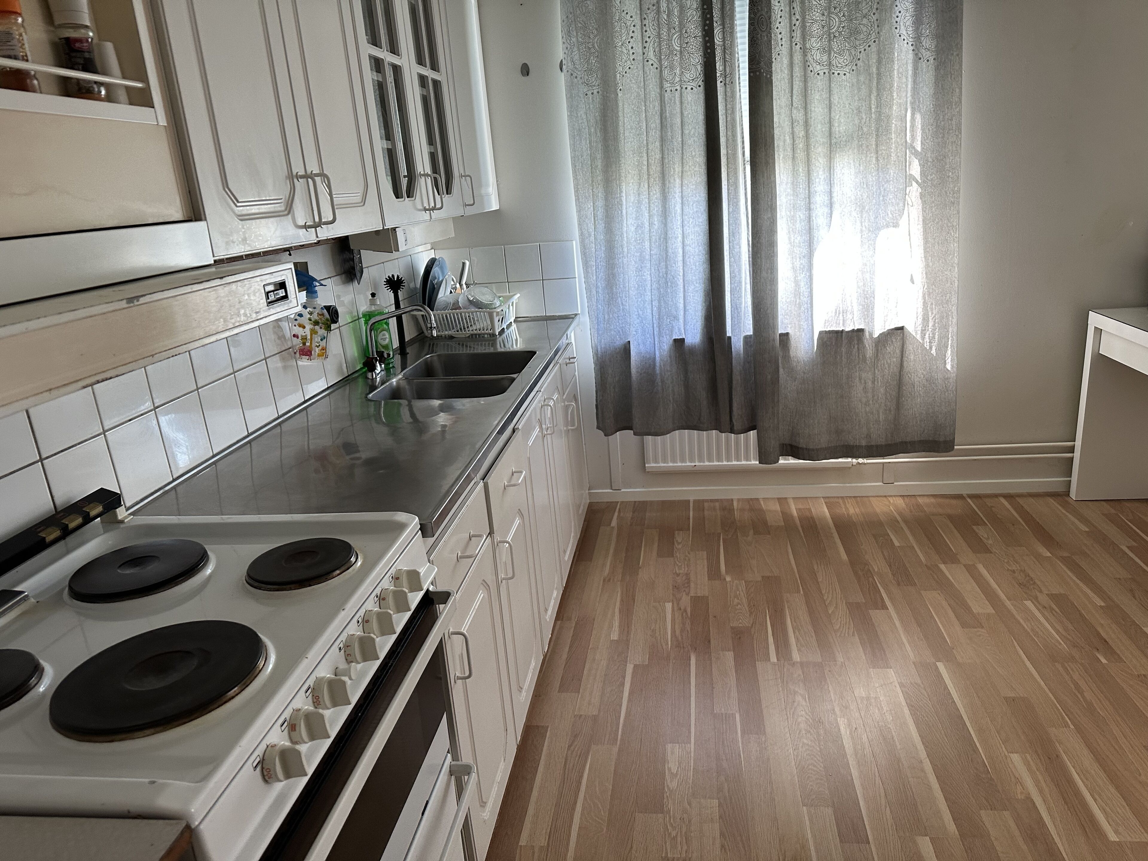 A kitchen with white cabinets, a stainless steel sink, and a stove.