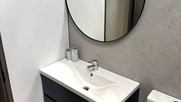 A modern bathroom with a white sink, black cabinet, and a round mirror.