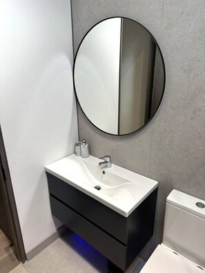 Un bagno moderno con un lavandino bianco, un mobile contenitore nero e uno specchio rotondo.