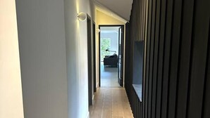 Een moderne hal met houten vloer, een donkere accentmuur en inbouwspots.